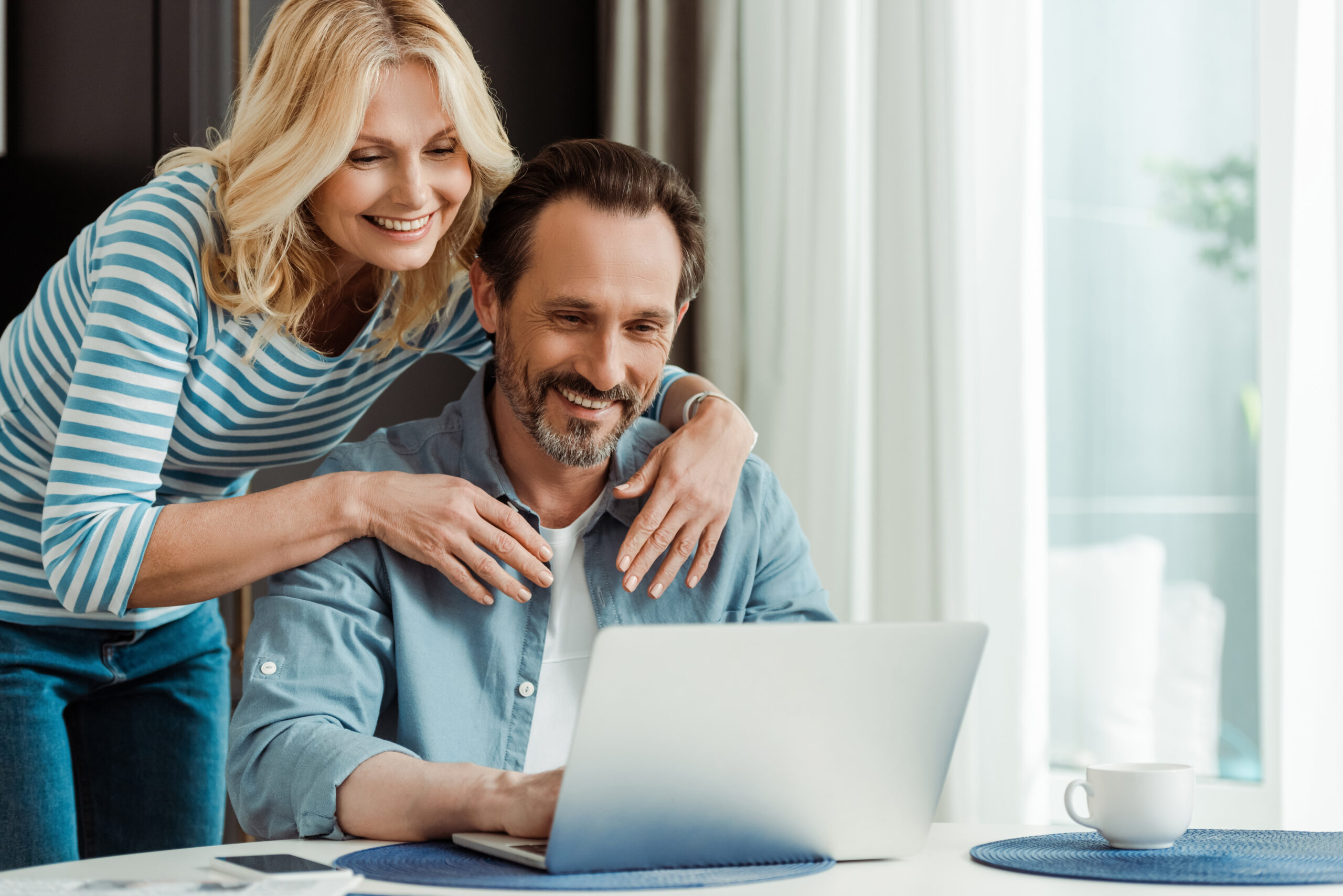 Selective focus of smiling woman embracing husband using laptop in kitchen Selective focus of smiling woman embracing husband using laptop in kitchen